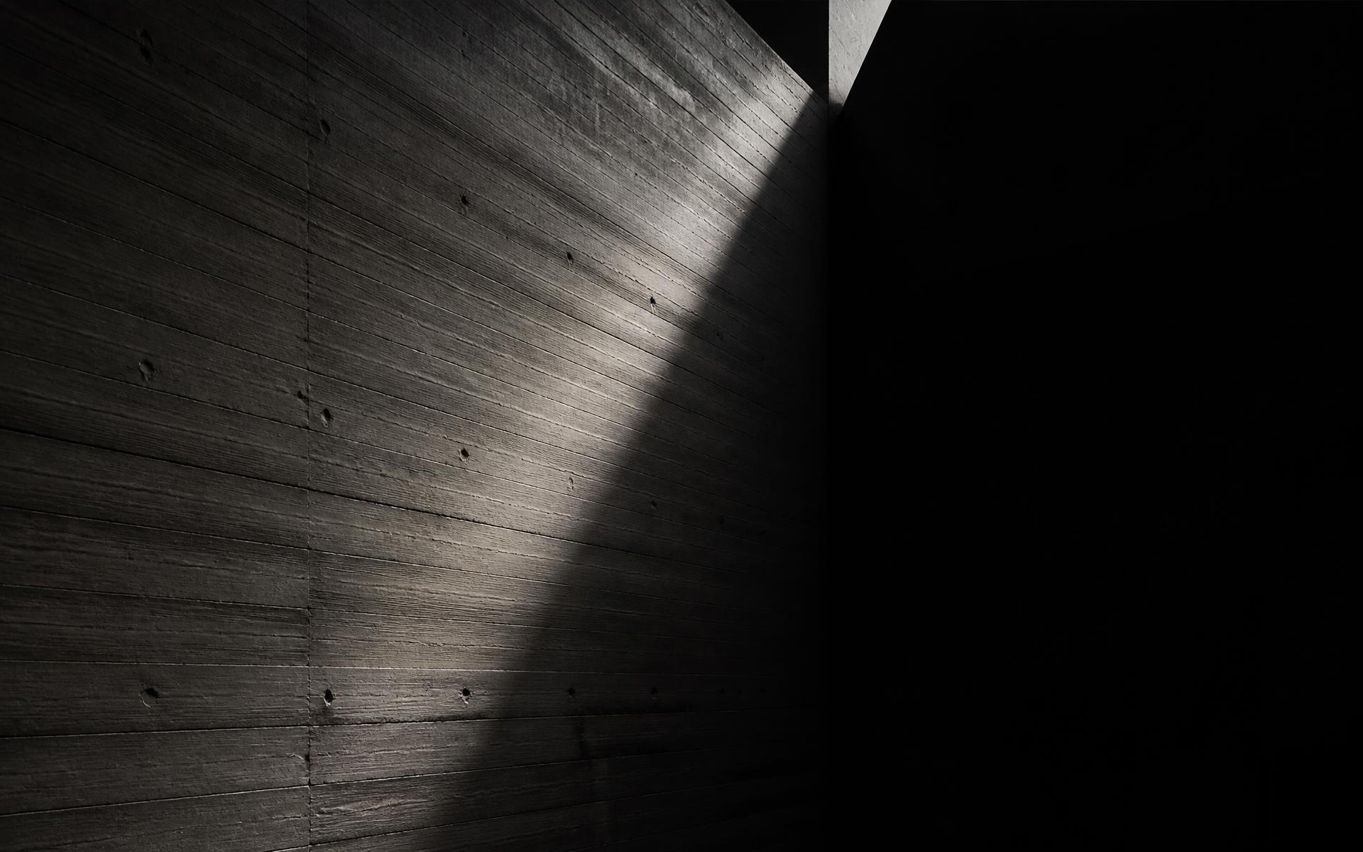 Board-formed concrete wall lit by a single blade of daylight